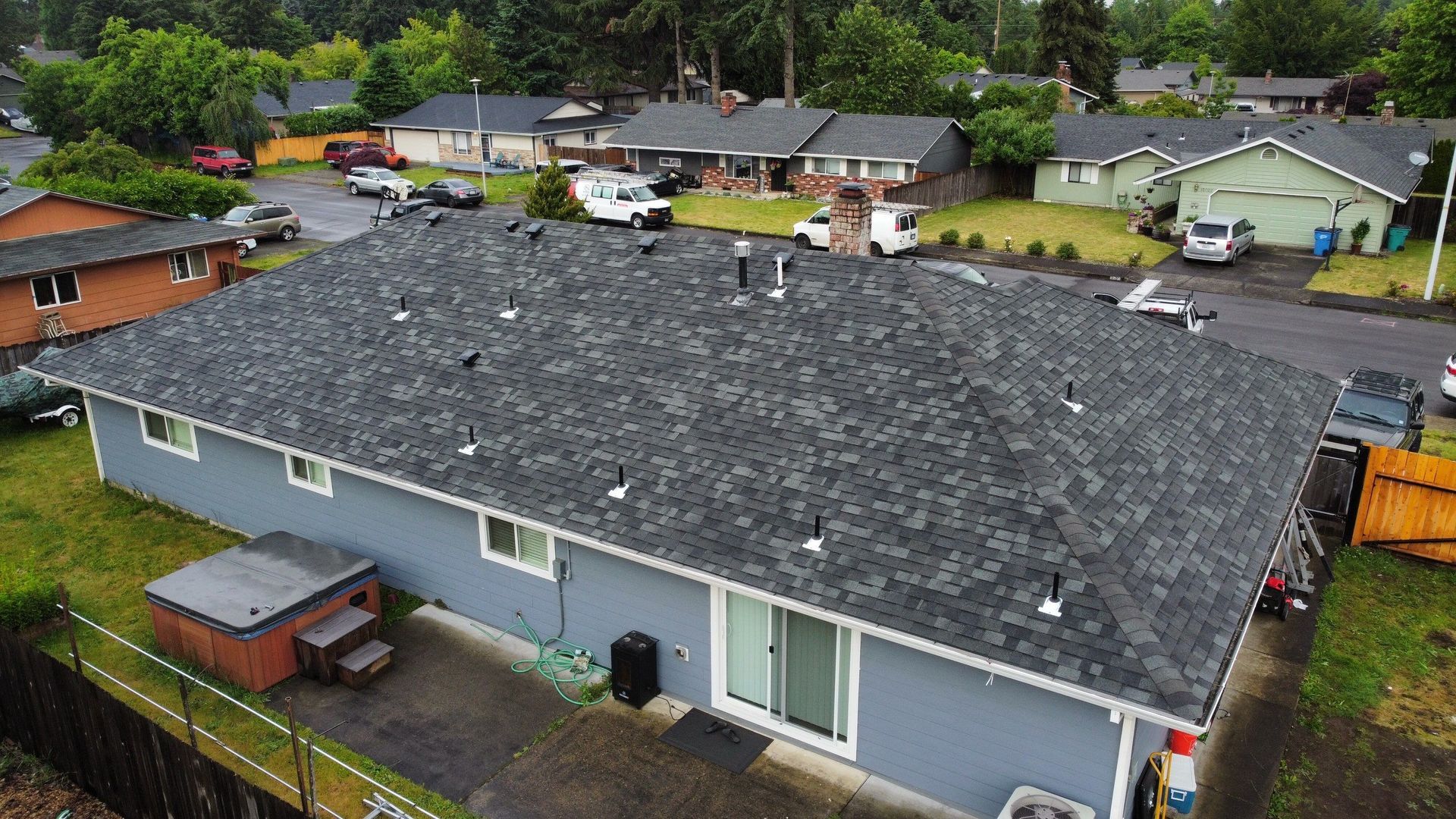 Blue house with new dark gray roof. Houses and cars in the suburban neighborhood.