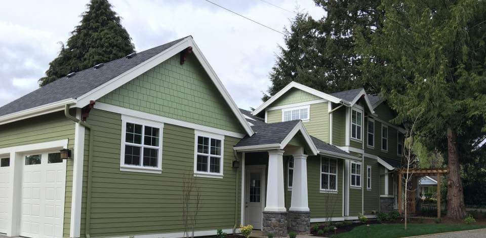 Green-painted house with white trim. Garage doors and front porch with pillars, cloudy sky.