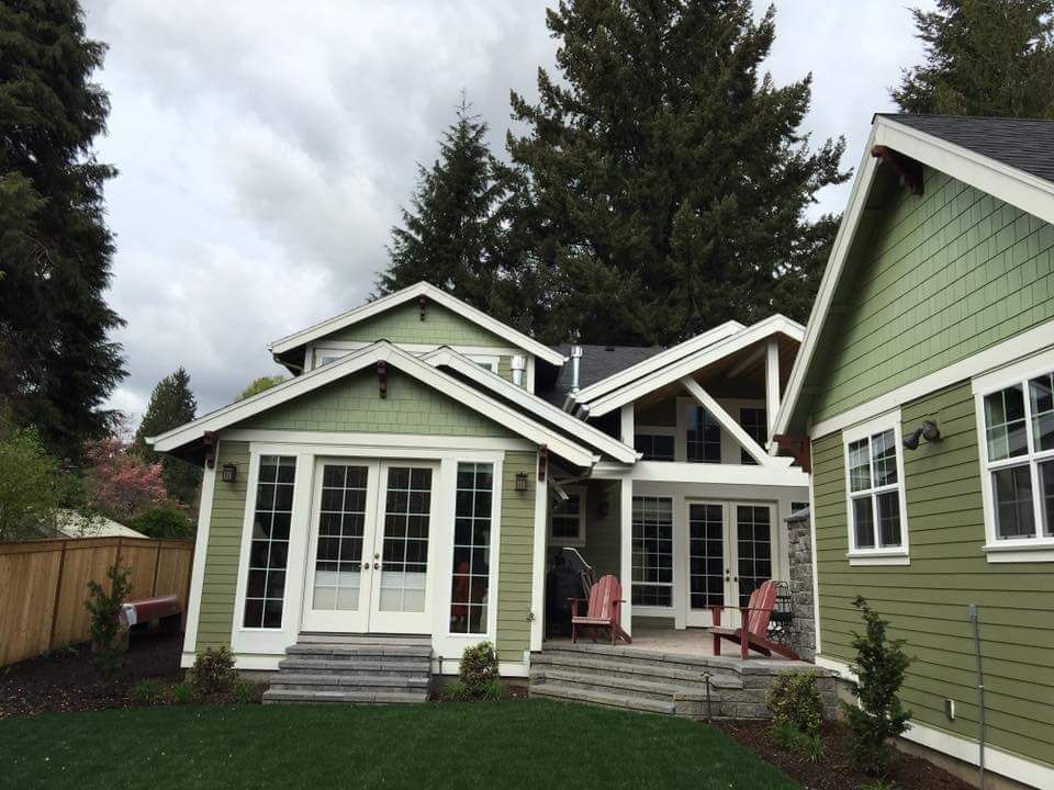 Green house with white trim, double doors, and stone steps. Red chairs on patio. Overcast day.