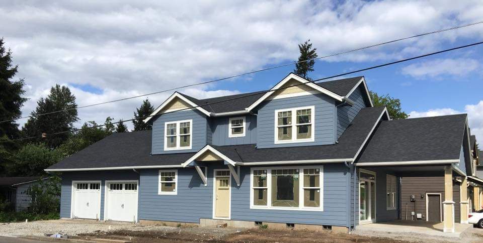 Blue house under construction with white trim, white garage doors, and blue siding.