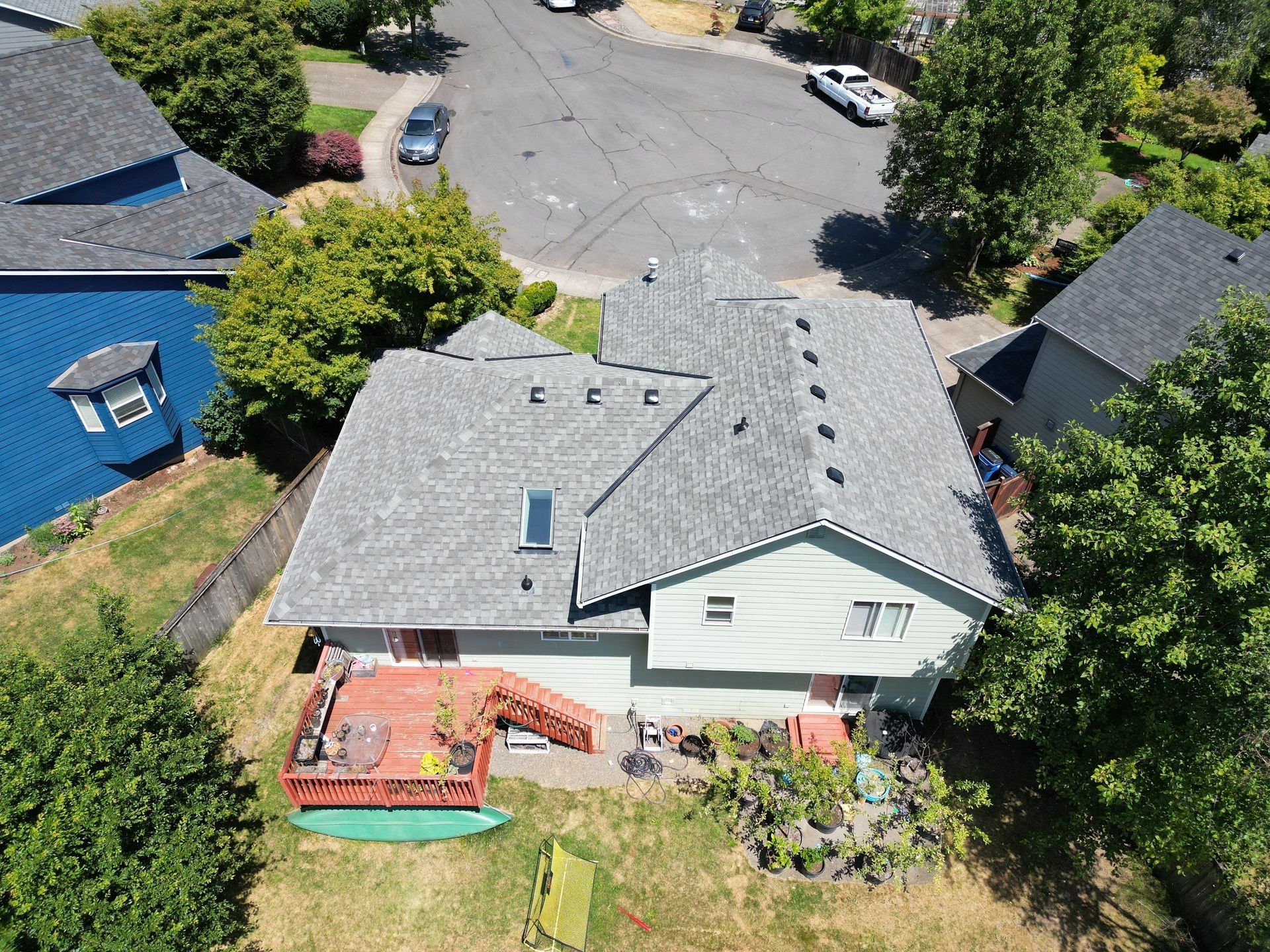 Aerial view of a gray-roofed house with a red deck in a residential neighborhood, surrounded by trees.