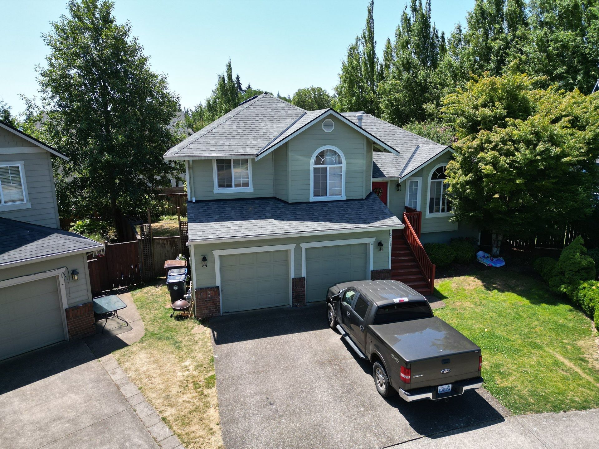 Two-story green house with a gray roof and a truck parked in the driveway on a sunny day.