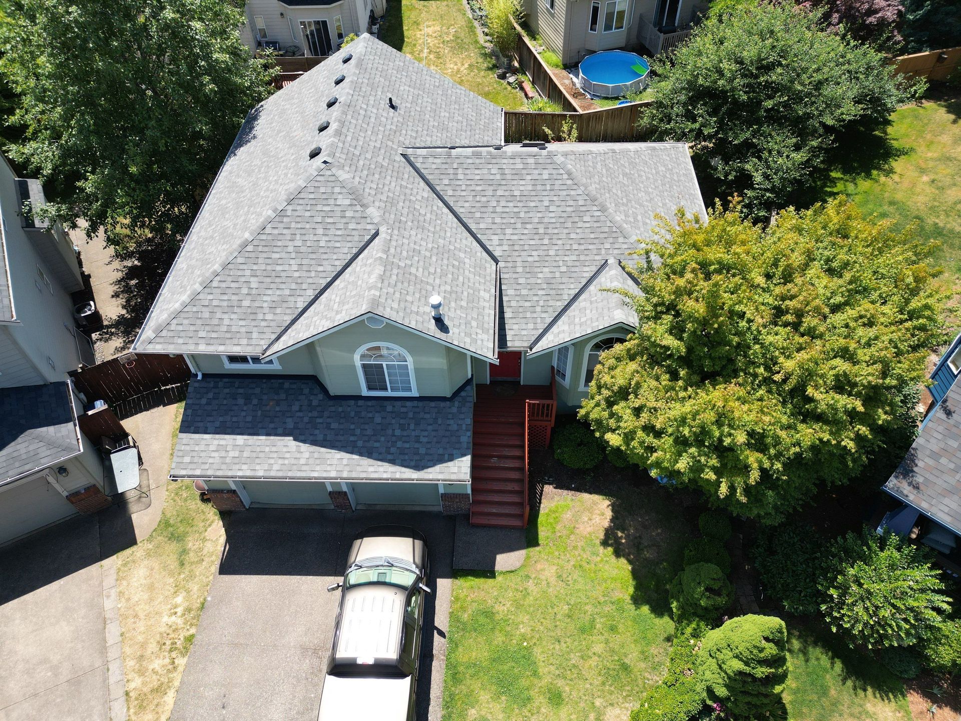 Aerial view of a house with a gray roof, green siding, and a driveway with a truck parked on it.