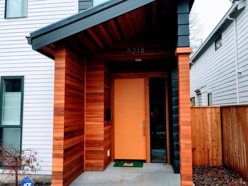 Orange door with wood accents on a modern home. Address is above door.