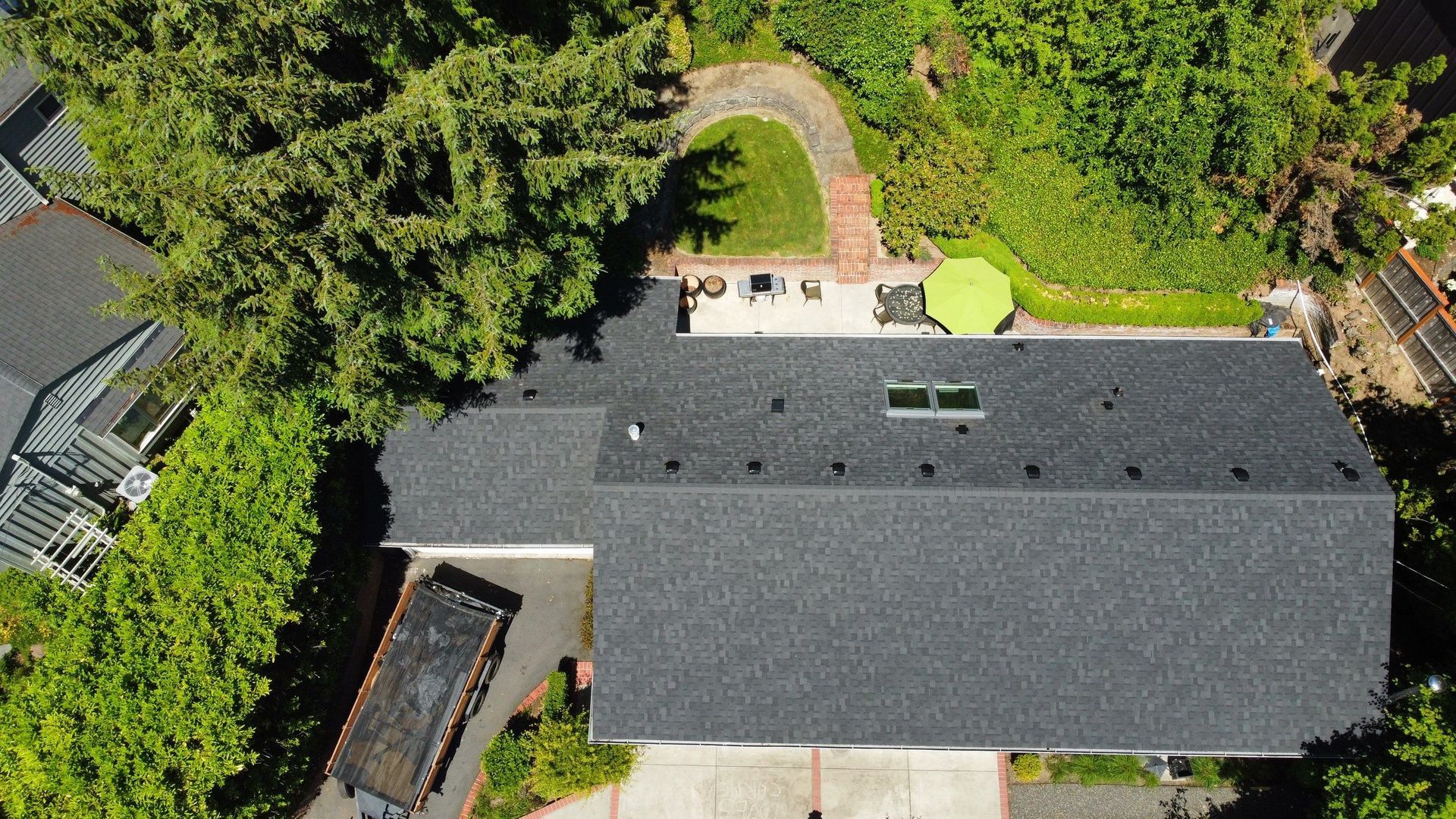 Overhead view of a house with a dark gray roof, surrounded by trees and a patio with a green umbrella.