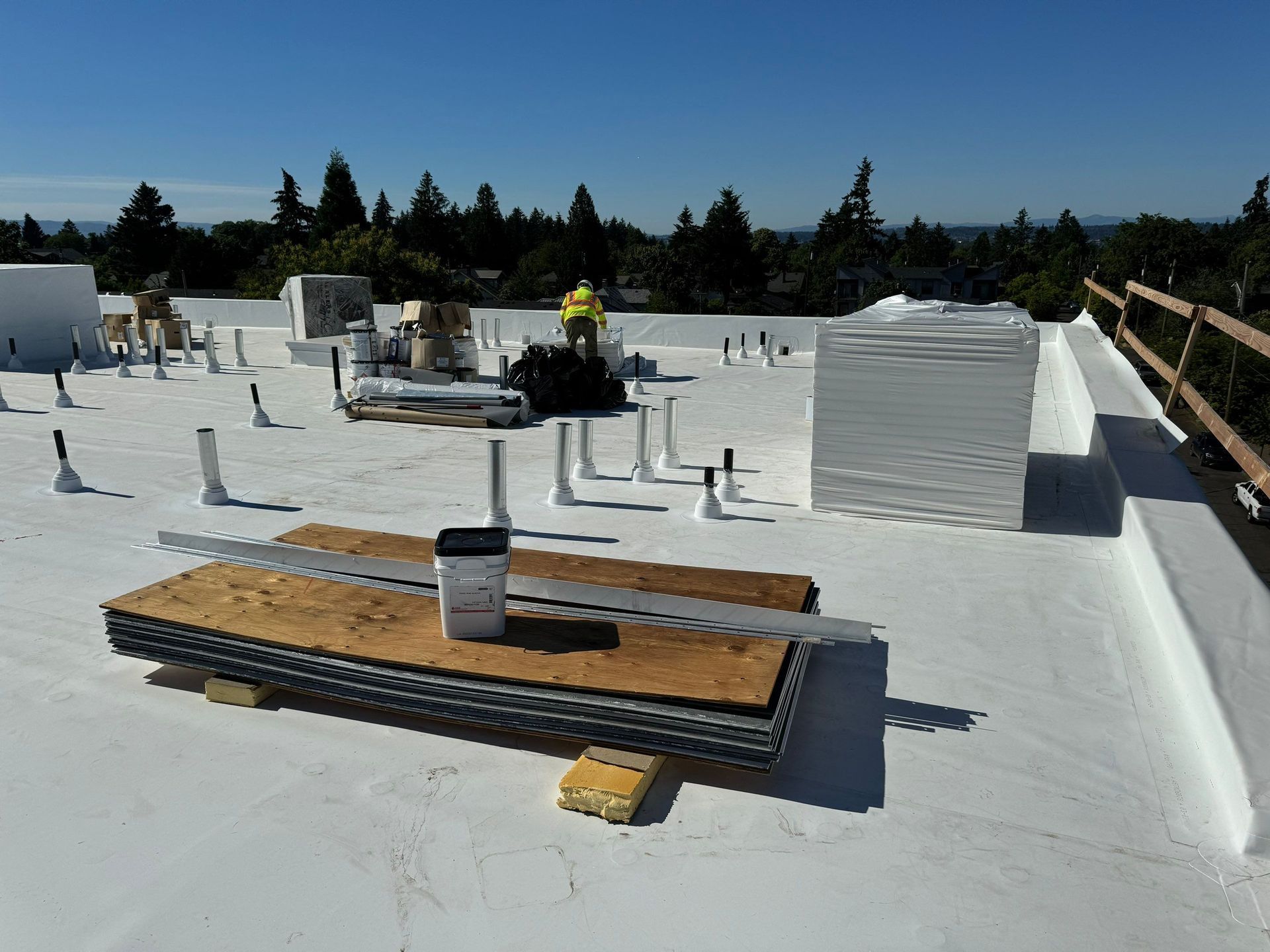 A flat roof under construction; white surface, tools, materials, and a worker visible on a sunny day.
