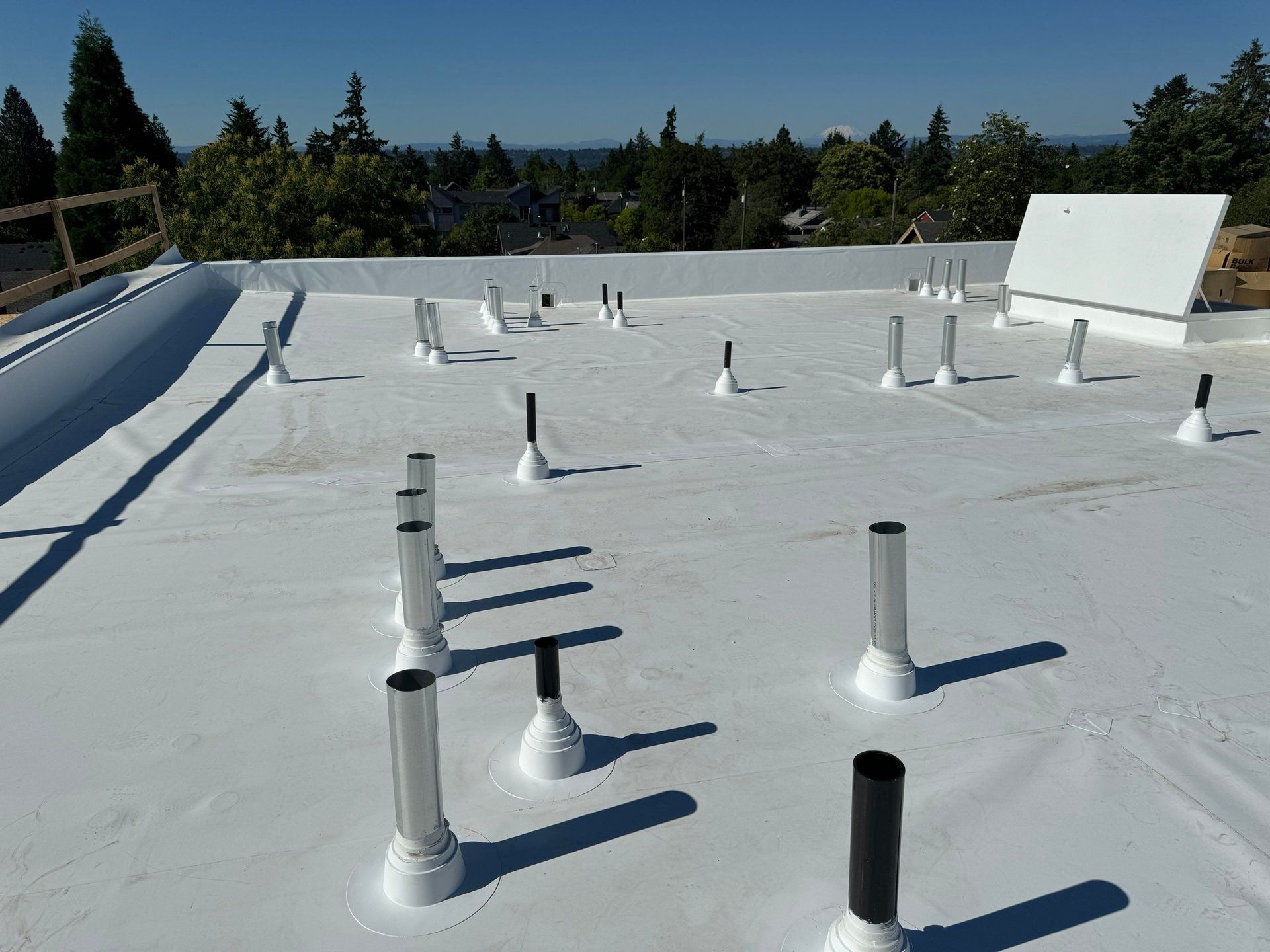 White flat roof with plumbing pipes and vents. Sunny day.