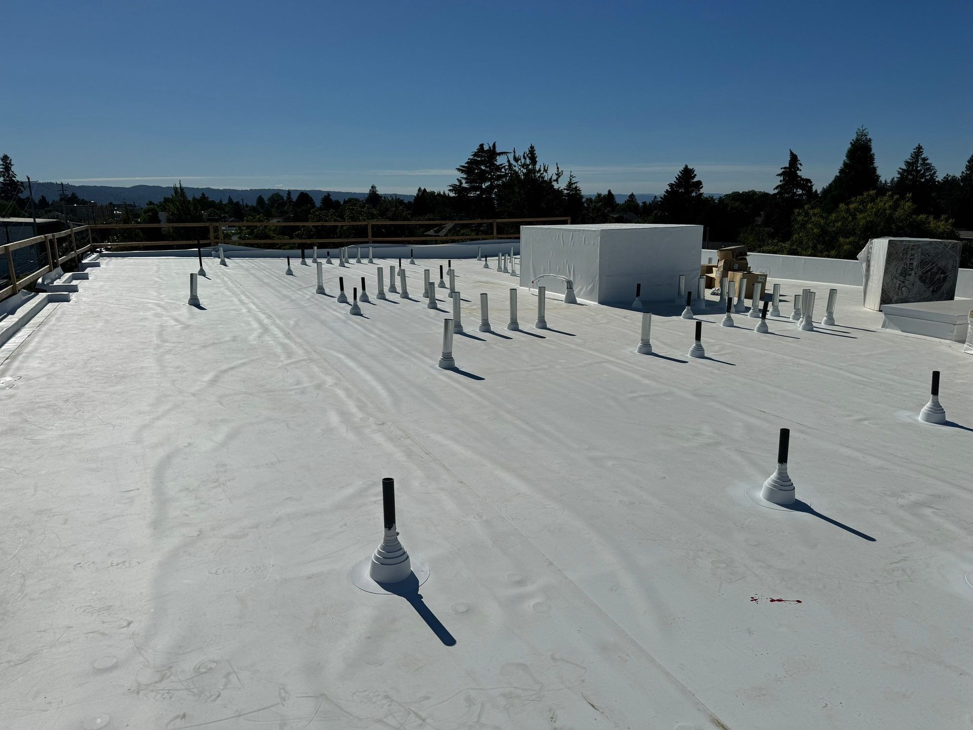 White flat roof with many pipes and a clear blue sky.