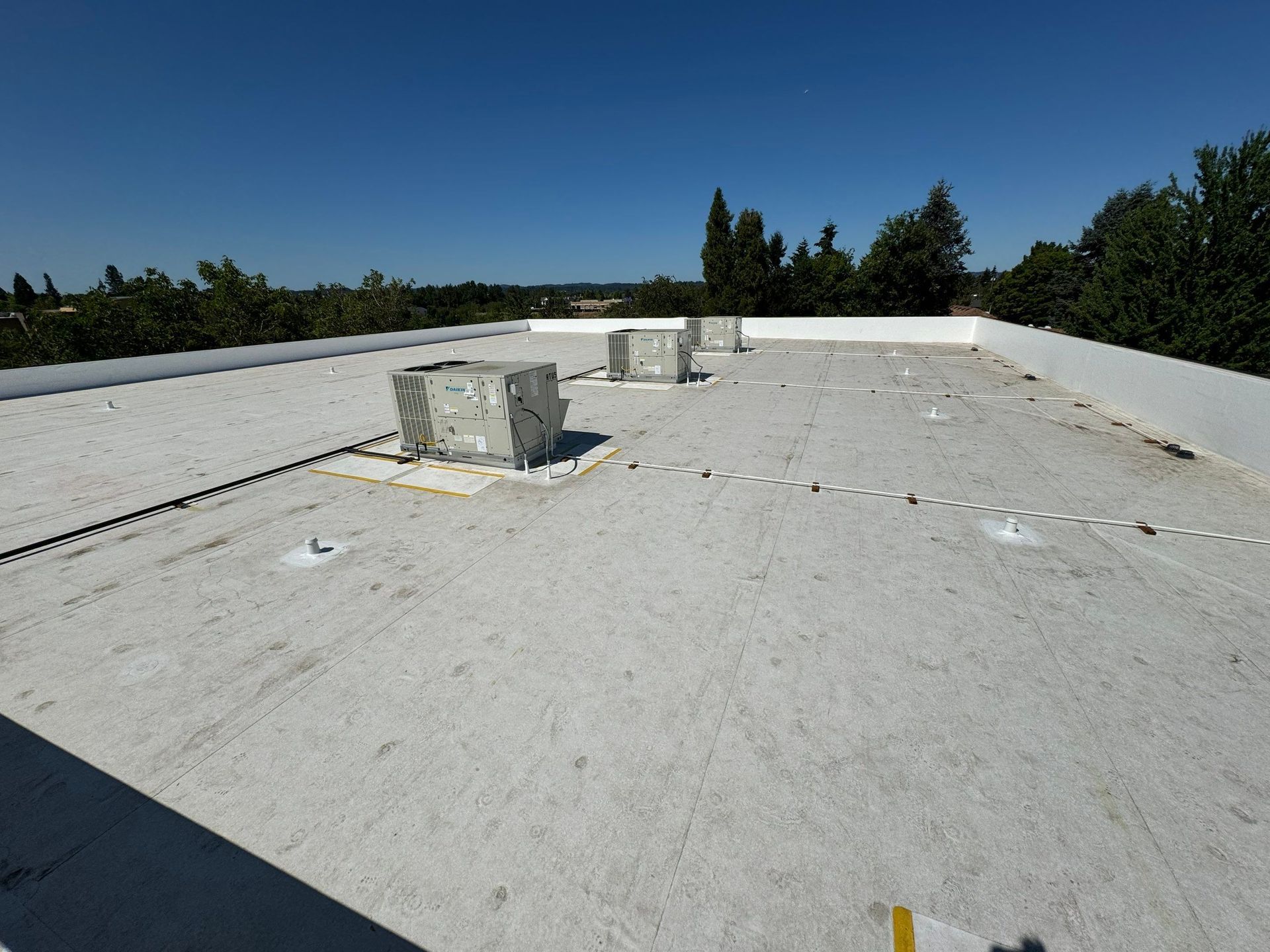 White rooftop with HVAC units, surrounded by trees under a clear blue sky.