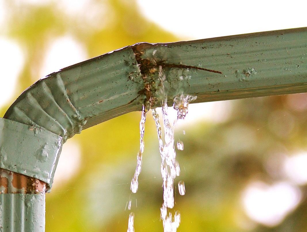 Green gutter with a leak, water pouring out.