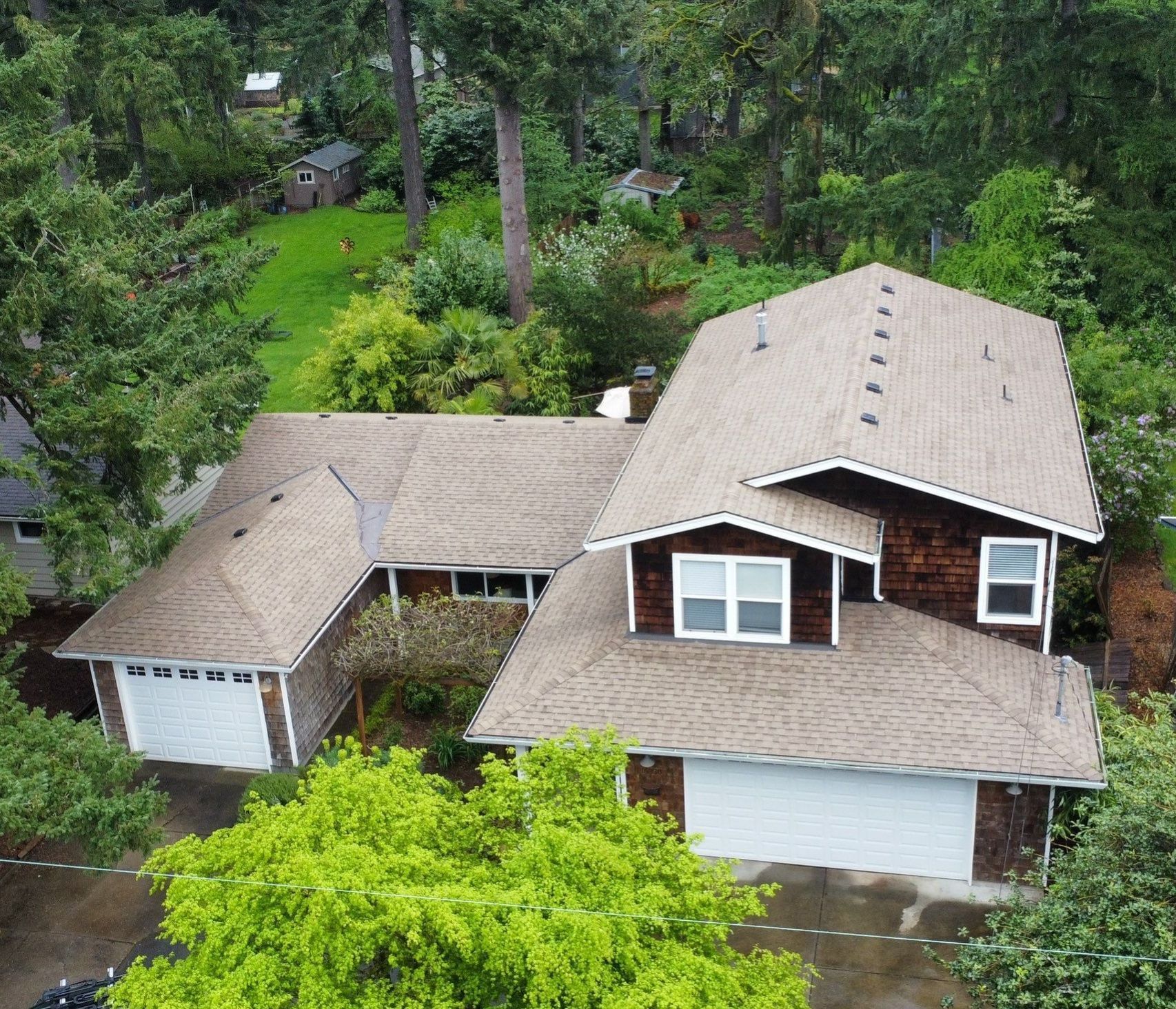 Aerial view of a brown-roofed house with a white garage door, surrounded by green trees.
