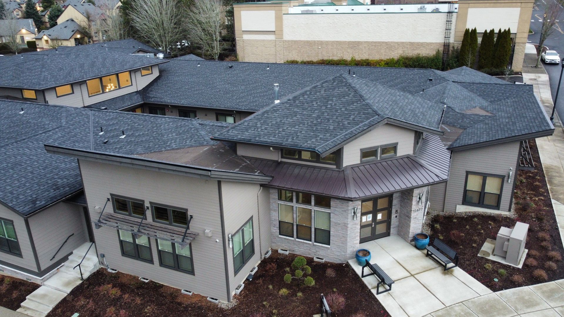 Modern building with gray exterior, dark roof, and landscaping.