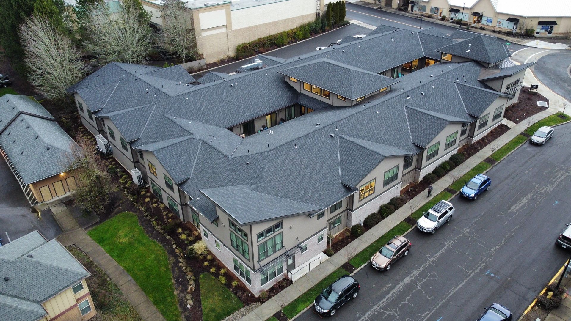 Aerial view of a modern gray apartment complex with dark gray roofs, parked cars line the street.