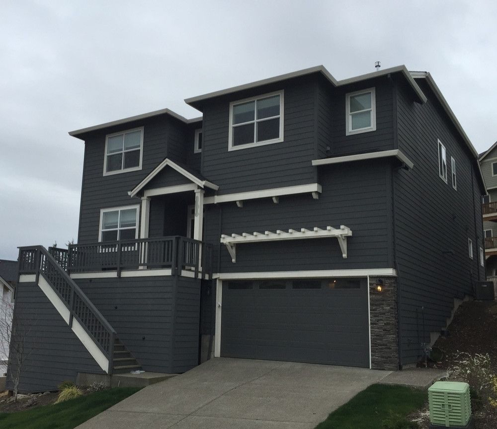 Two-story gray house with attached garage, elevated deck, and front stairs on an overcast day.