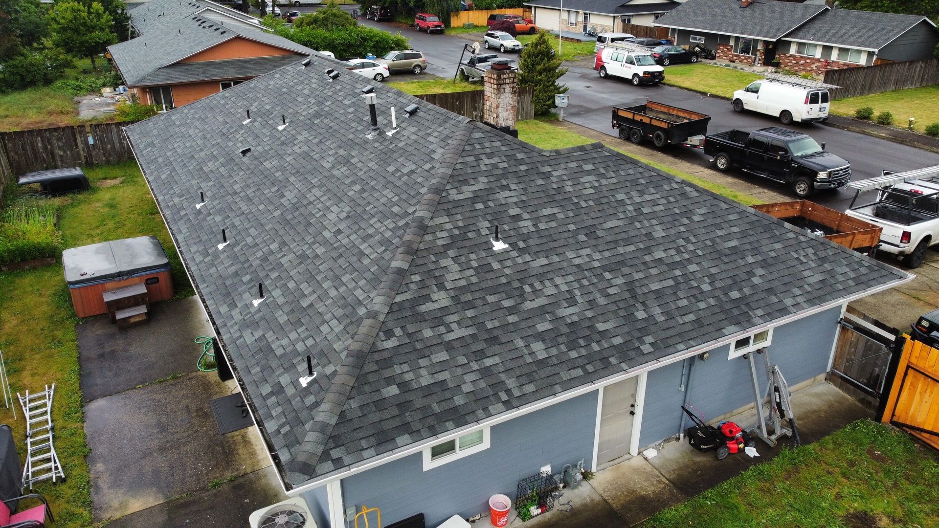 Overhead view of a house with a newly shingled roof. Cars and a truck are parked in the street.