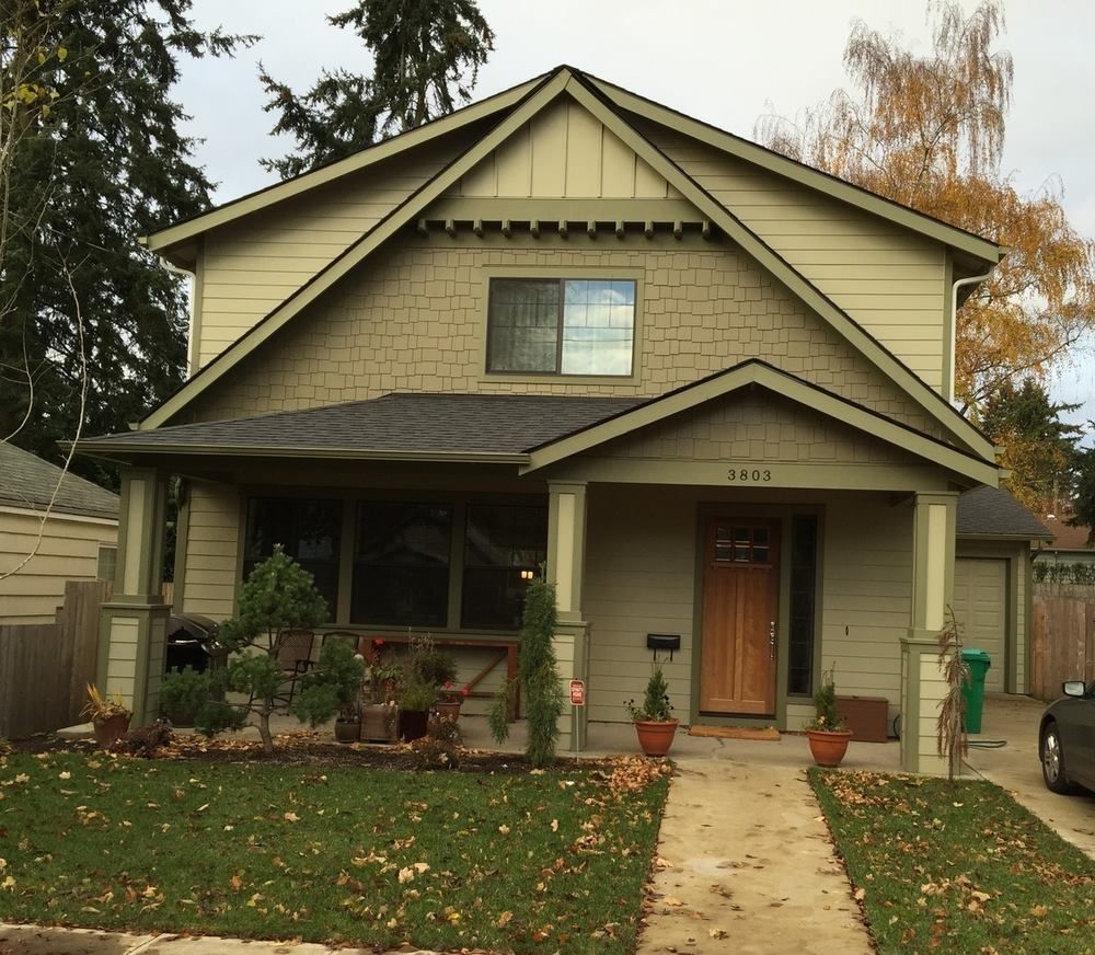 Two-story house with a green exterior, covered porch, and a small front yard with trees and bushes.