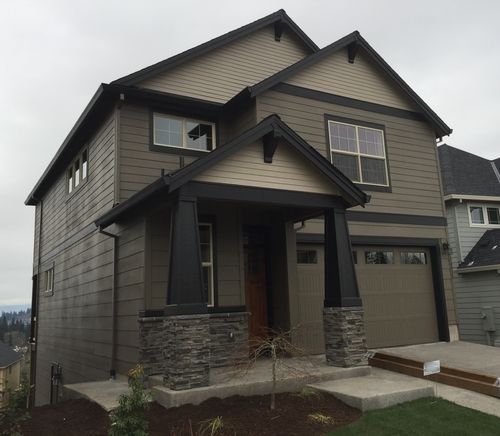 Two-story house with tan siding, black trim, stone accents, and a covered porch.