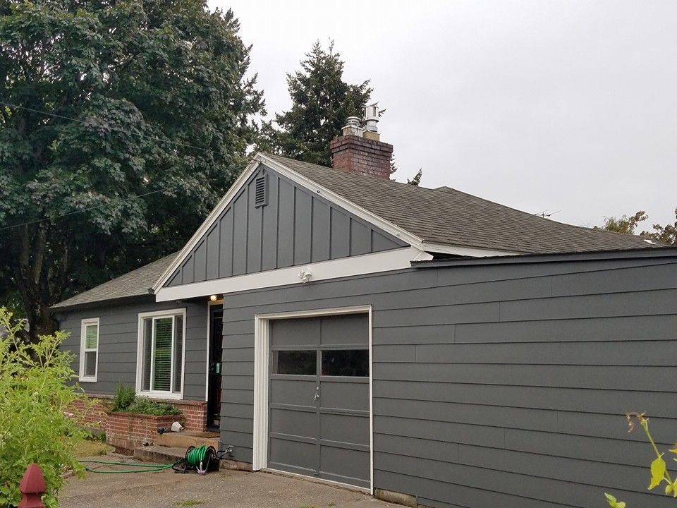 Gray house with a garage, brick chimney, and overcast sky.
