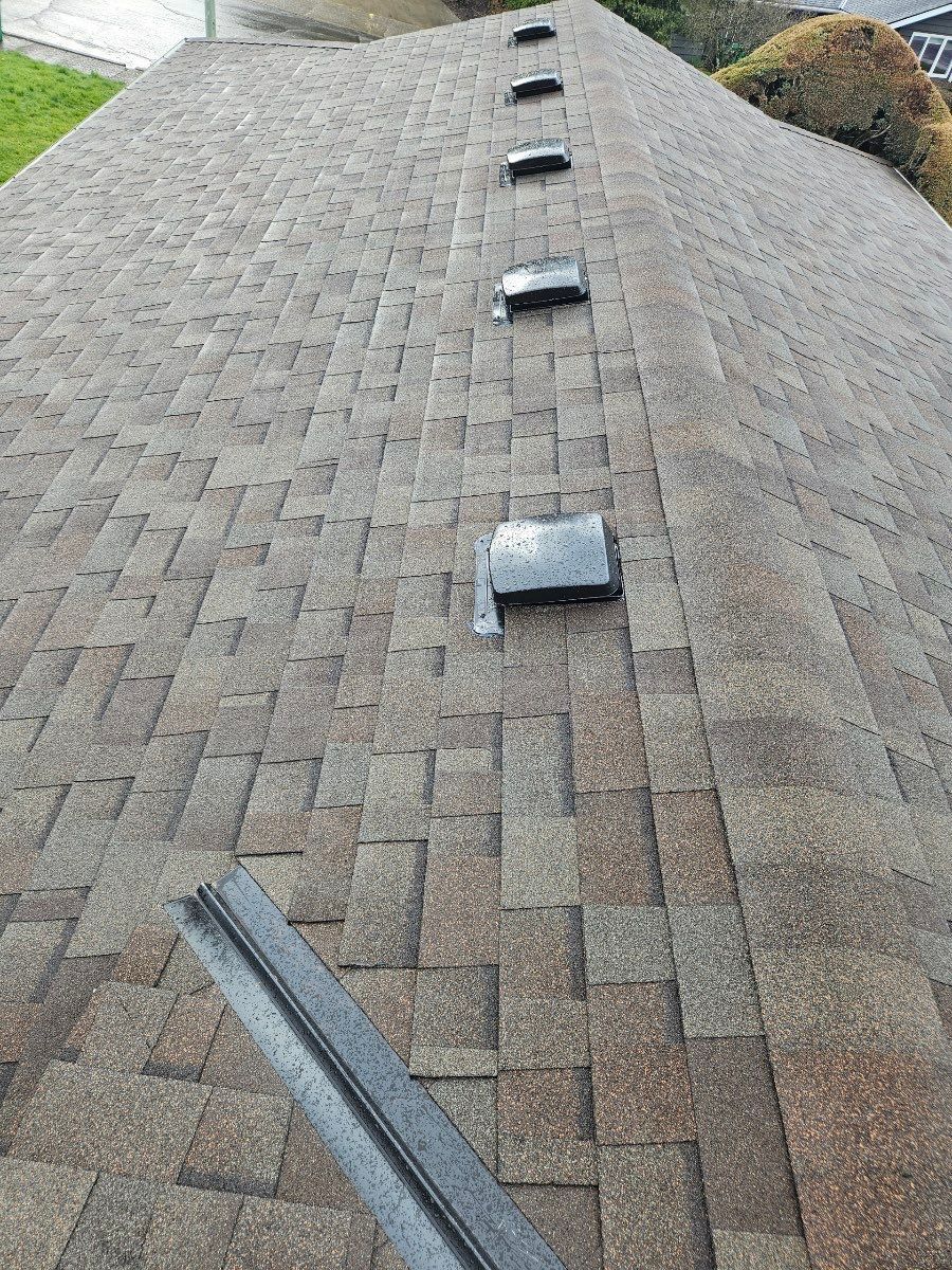 Brown shingled roof with vent stacks. A metal flashing strip rests in the foreground.