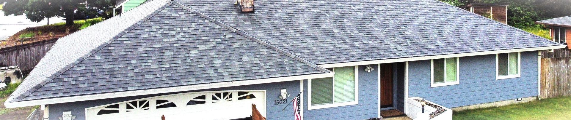 Gray asphalt shingle roof on a house with a gutter and surrounding greenery.