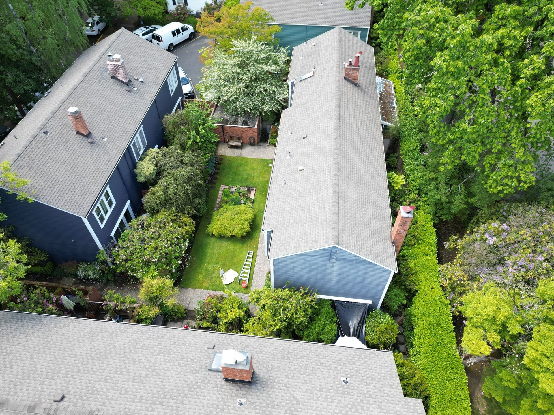 Aerial view of houses with gardens and trees; blue, grey, and green tones.