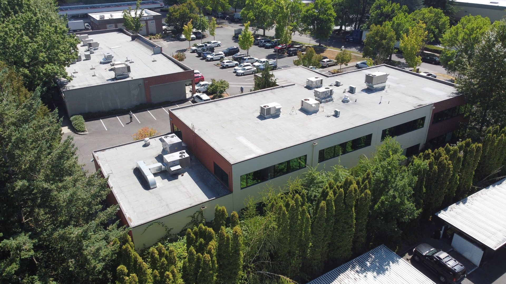 Aerial view of two-story commercial buildings with flat roofs, surrounded by trees and a parking lot.