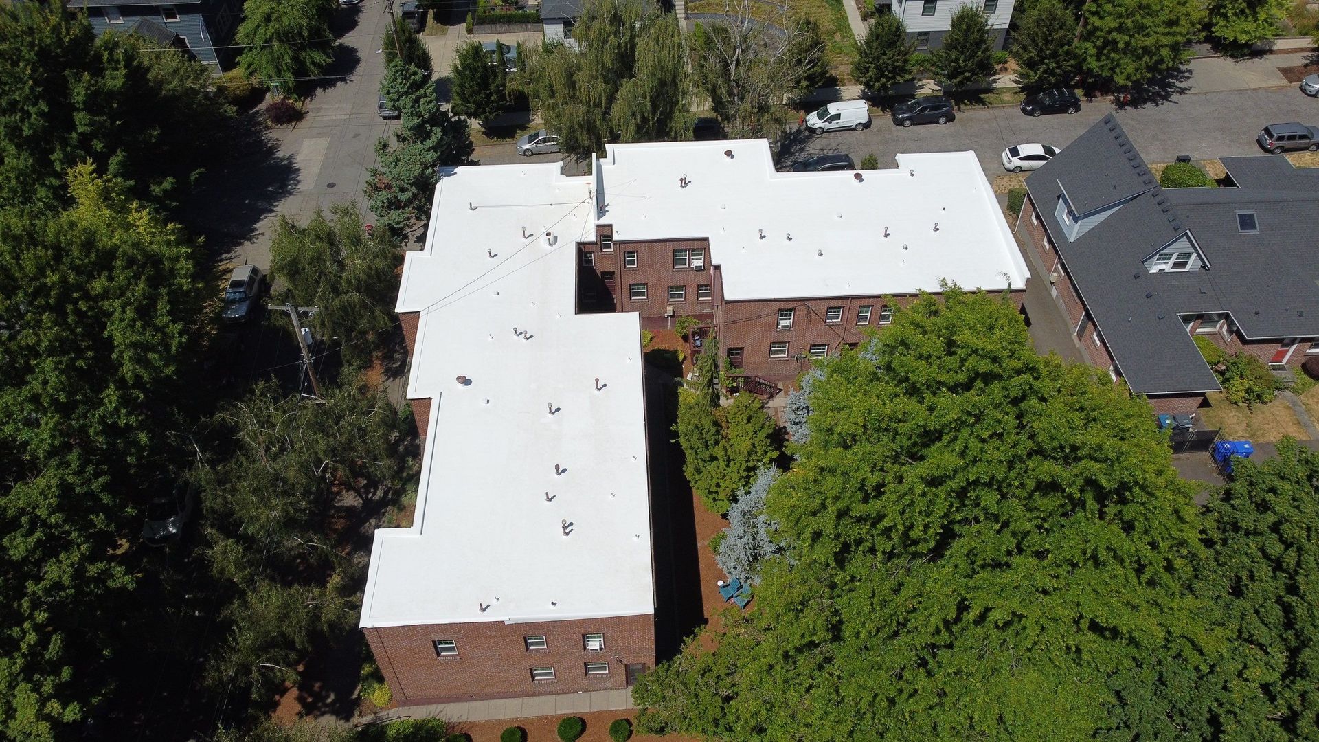 Aerial view of a red brick apartment building with white rooftops surrounded by trees and other buildings.