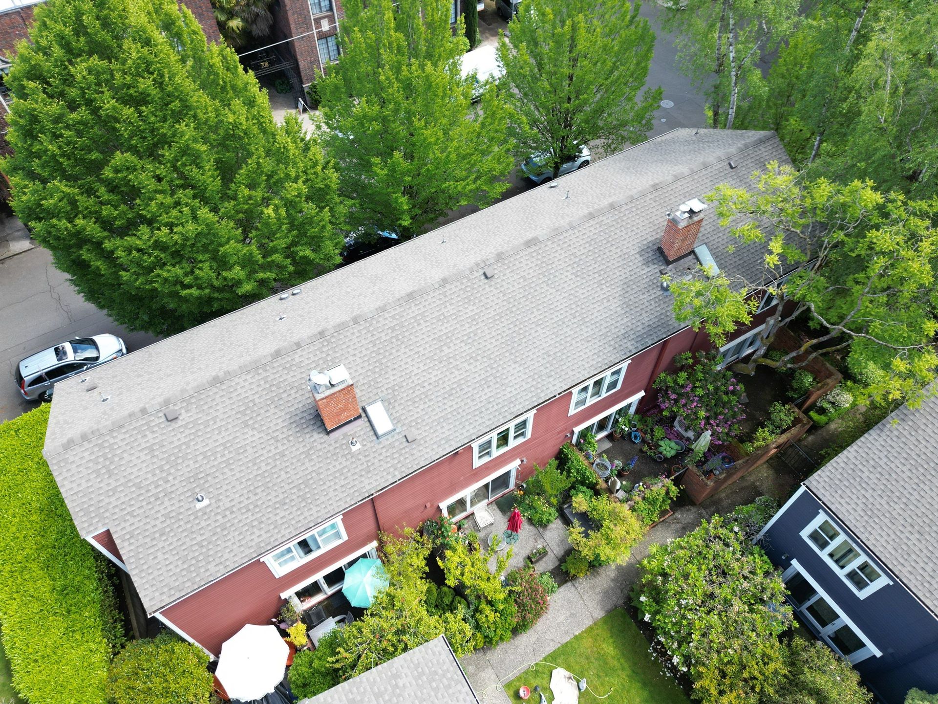 Aerial view of a red house with a gray roof, surrounded by green trees and a garden.
