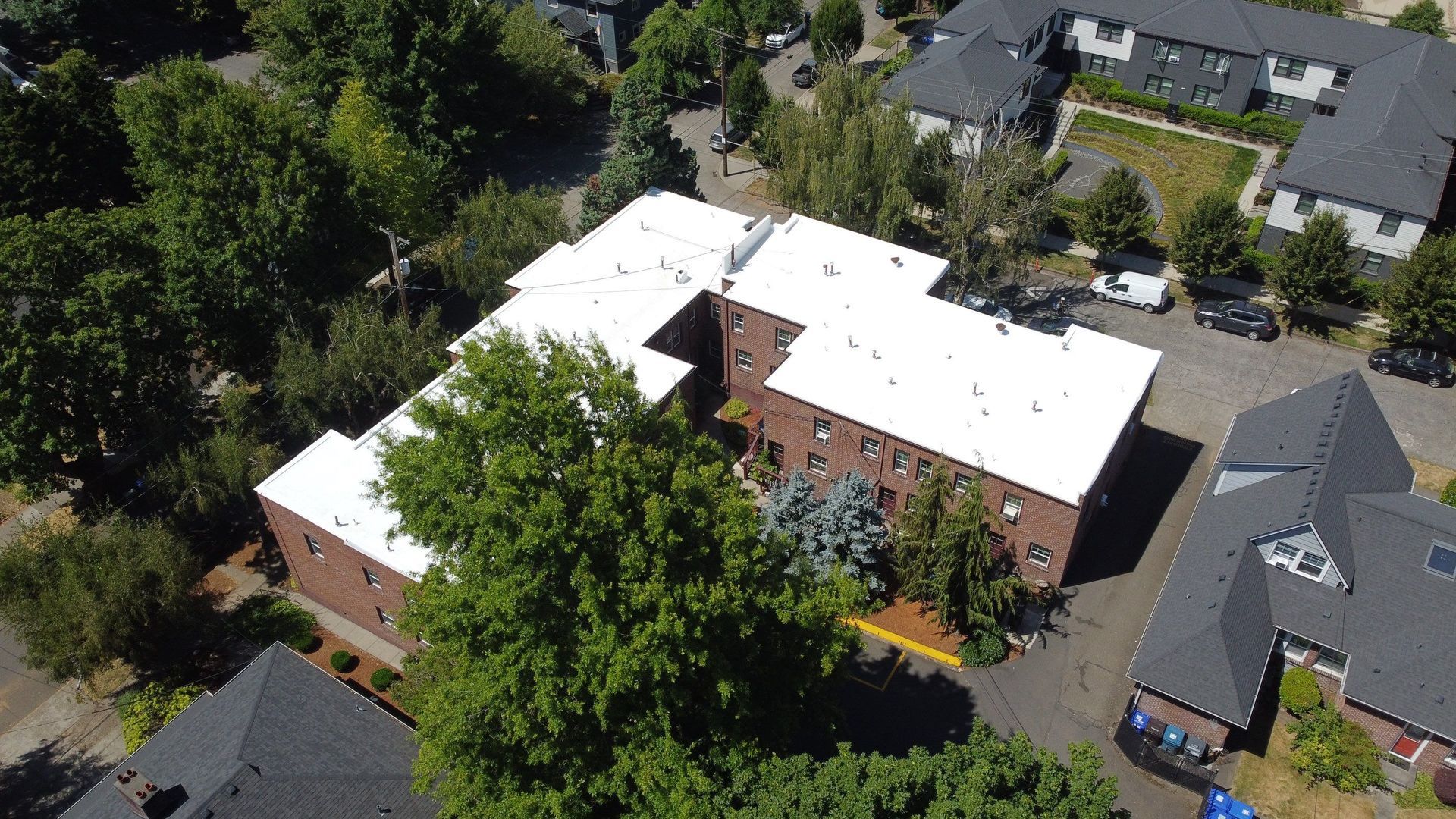 Aerial view of a brick apartment building with white roofs, surrounded by trees and other buildings.