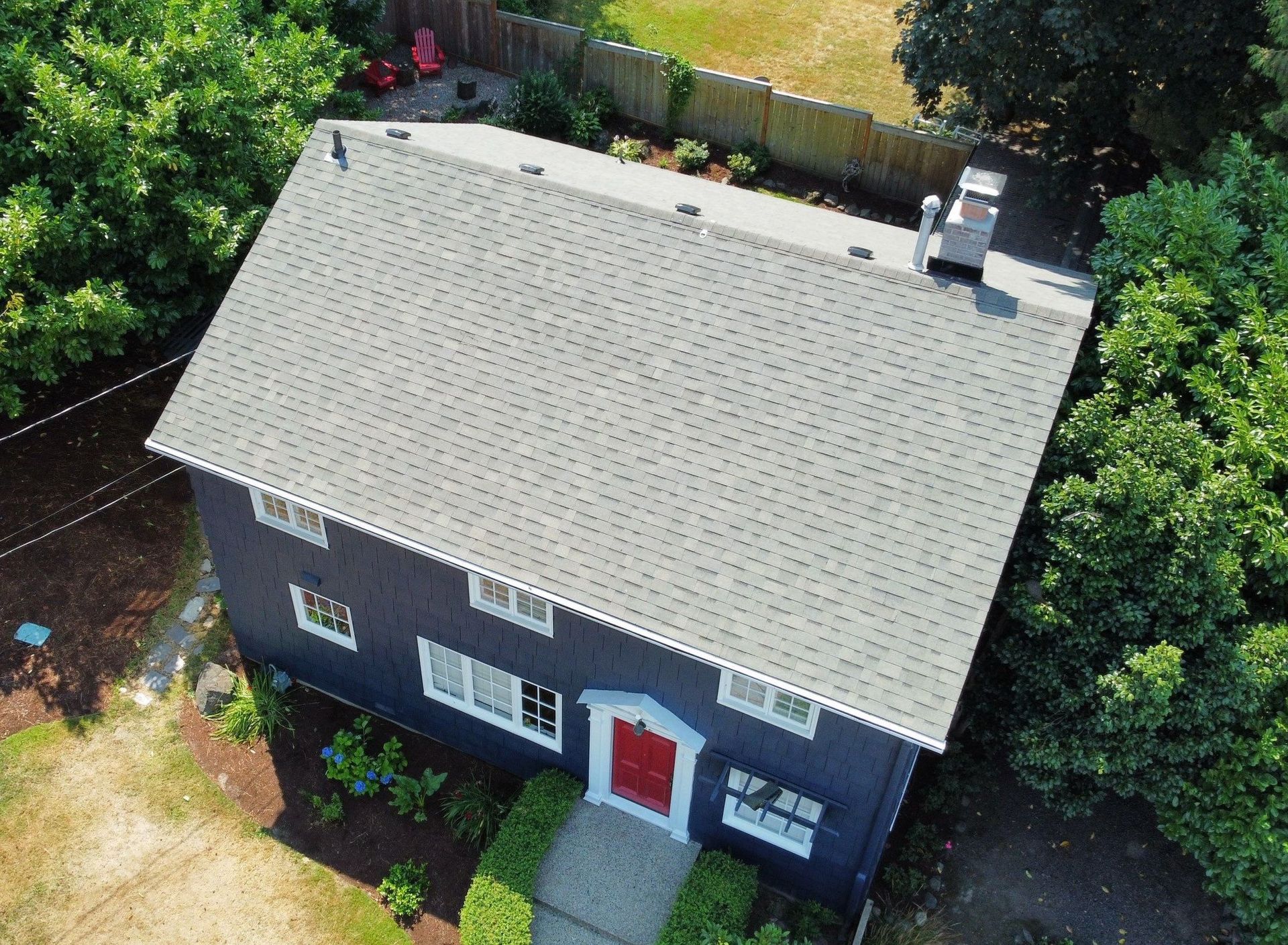 Dark blue house with gray roof, red door, surrounded by green trees and a backyard.