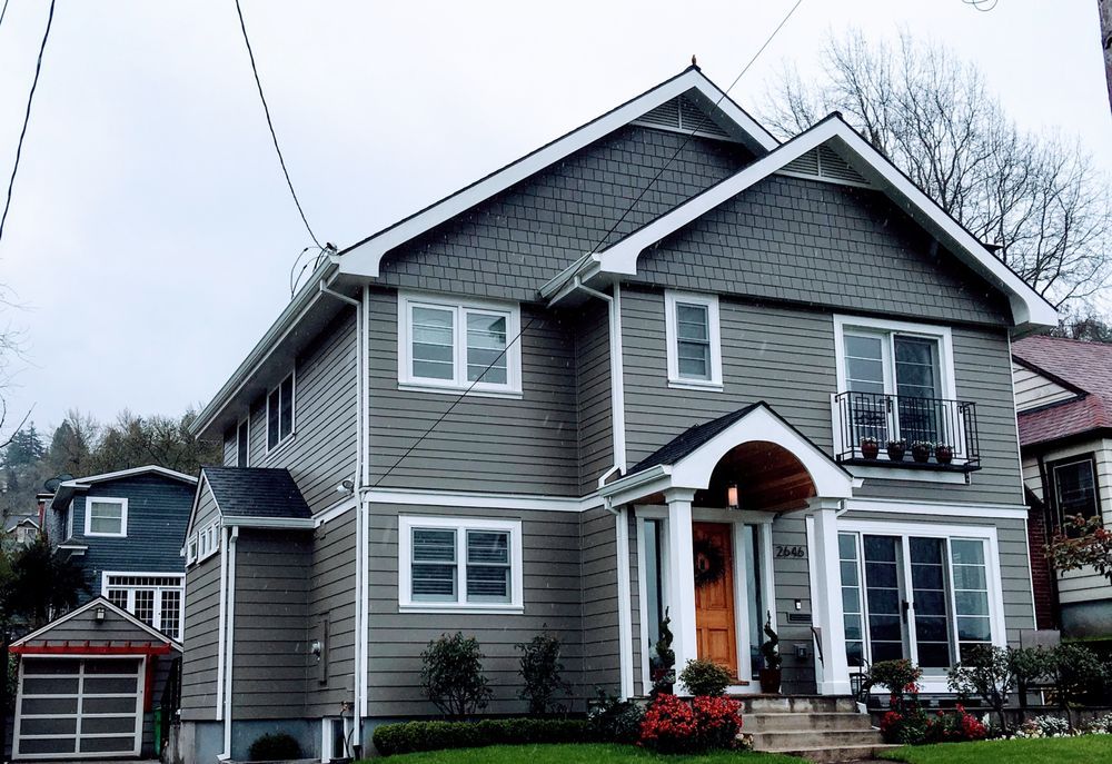 Two-story gray house with white trim and an orange front door, surrounded by other houses and trees.