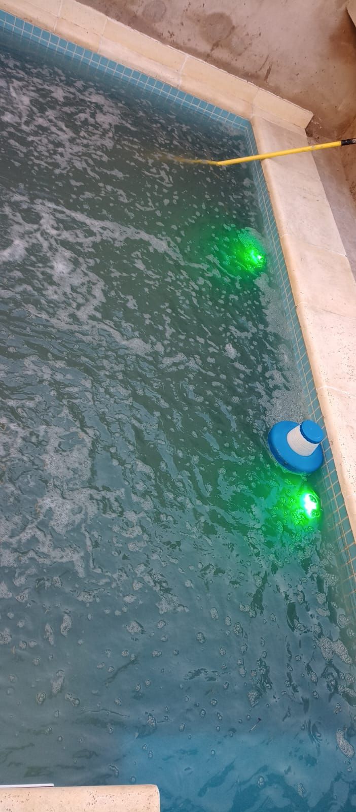Una piscina con luces verdes y un flotador azul. El agua ondula.