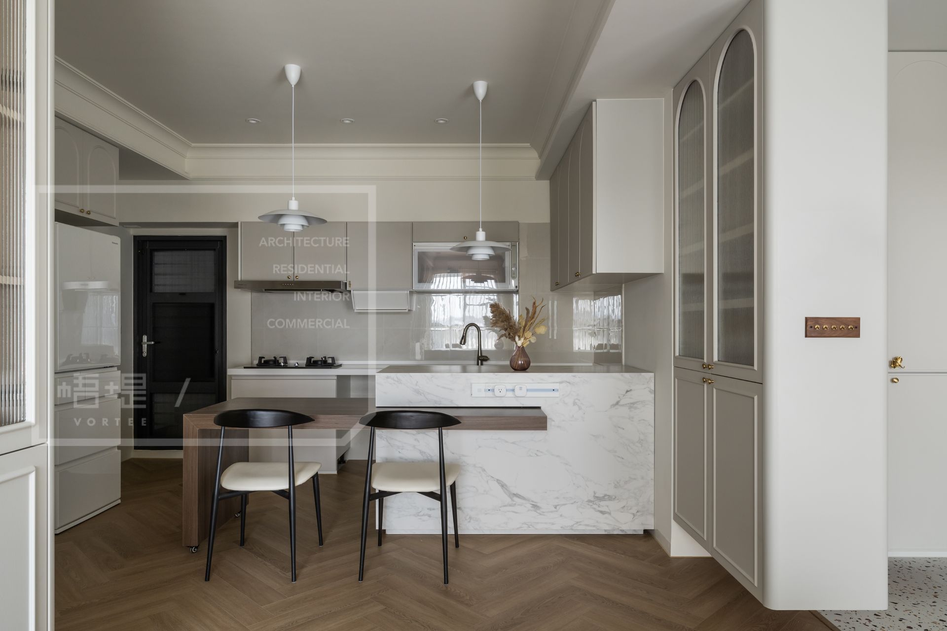 小坪數中島廚房設計範例：台南梧堤空間設計完美示範中島與餐桌結合的高效能配置。透過質感大理石紋吧檯延伸木質餐桌，搭配優雅的拱形長虹玻璃高櫃與溫潤人字拼木地板，在滿足海量收納與流暢料理動線的同時，極大化放