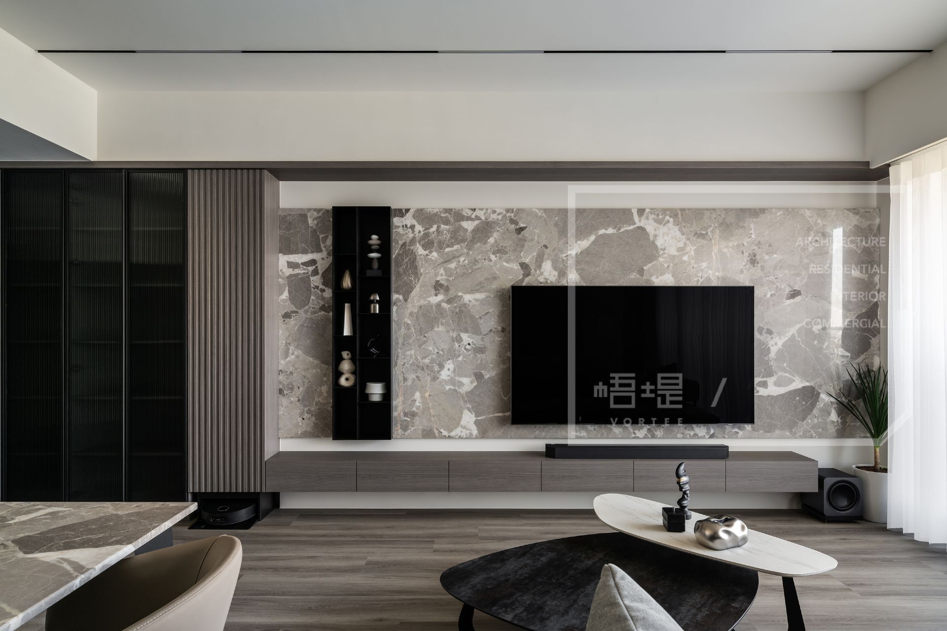現代簡約大氣客廳，灰色大理石紋電視牆搭配灰色懸空長櫃。左側木紋格柵與黑色玻璃高櫃相間，大螢幕掛壁電視居中。前景現代茶几與虎尾蘭盆栽裝飾，營造時尚家居。
