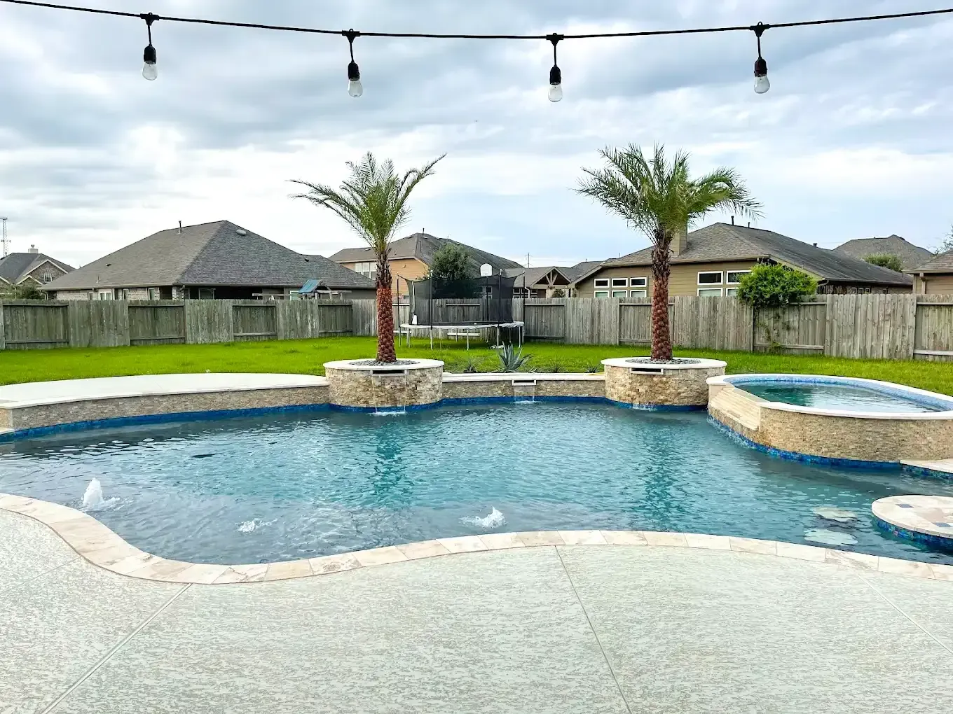 A large swimming pool with palm trees in the backyard of a house.