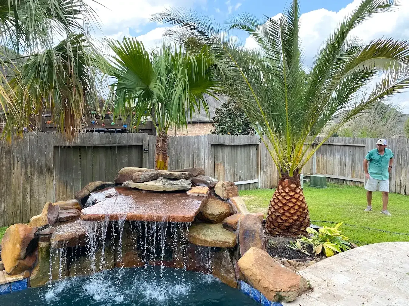 A man is standing in front of a waterfall in a backyard.