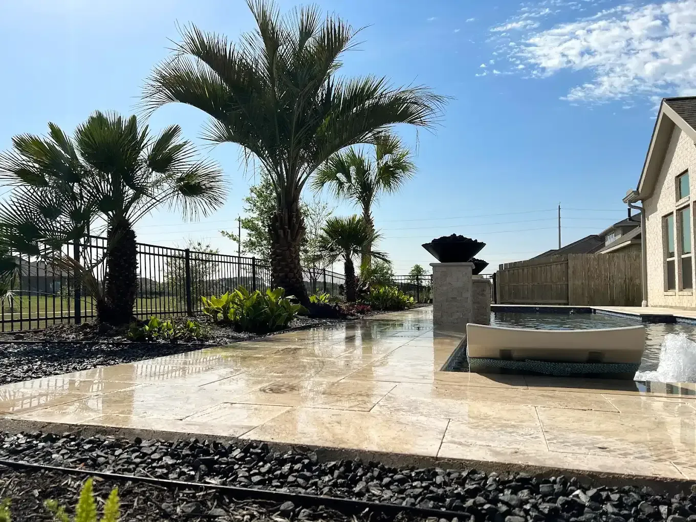 A patio with palm trees and a fountain in front of a house.