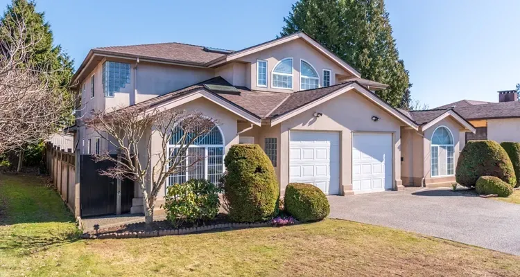 Two-story beige house with a brown roof and arched windows; driveway and grassy lawn.
