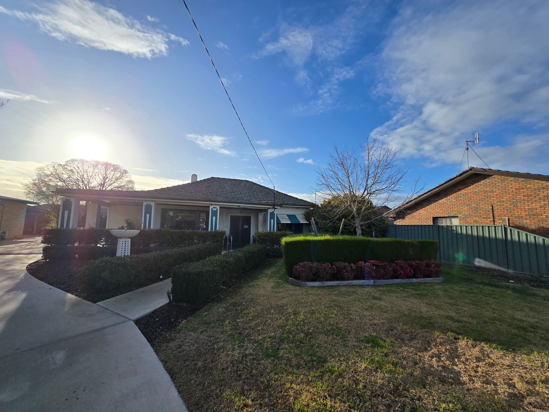 House with green hedge, brown roof, and blue sky.