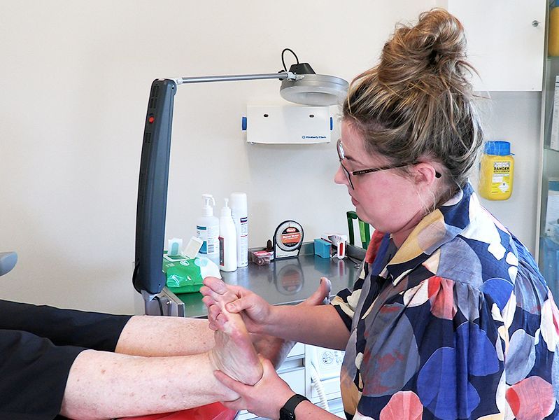 Woman in glasses examining patient's foot, medical setting.
