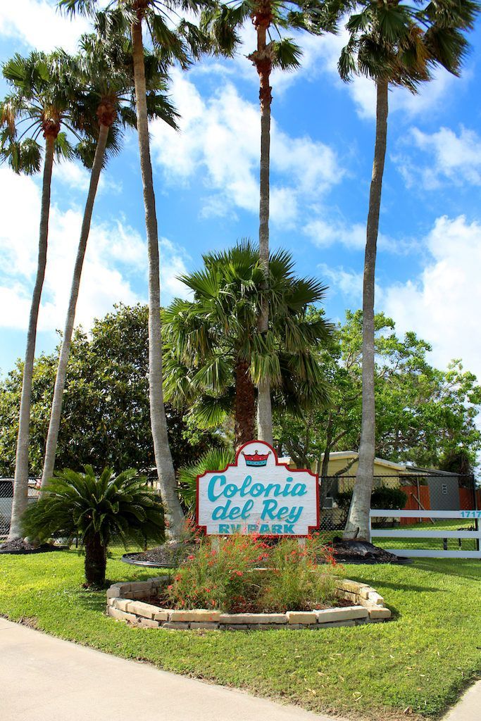 A sign for colonia del rey is surrounded by palm trees