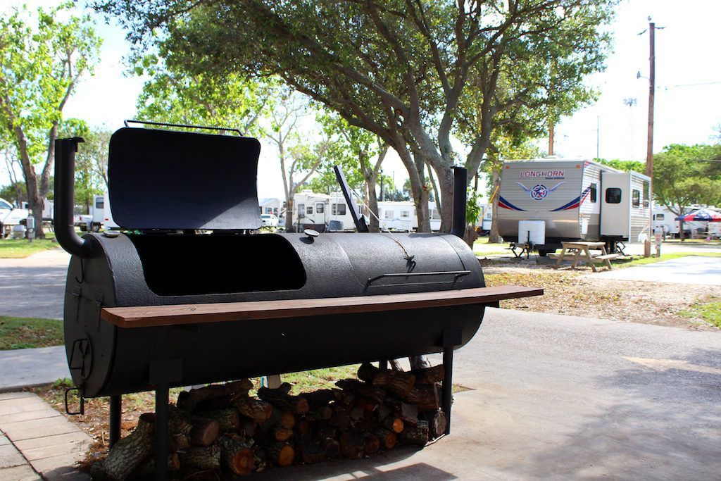 A bbq grill is sitting on a sidewalk next to a trailer.