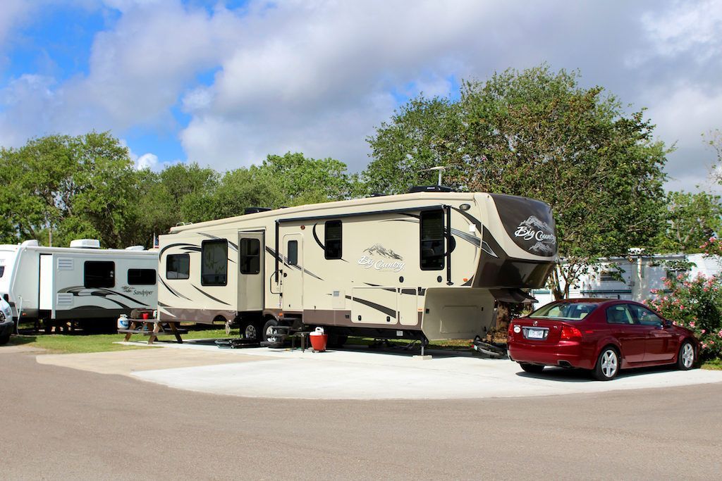 A red car is parked next to a rv in a parking lot.