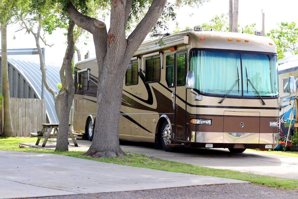 A large rv is parked under a tree in a parking lot.
