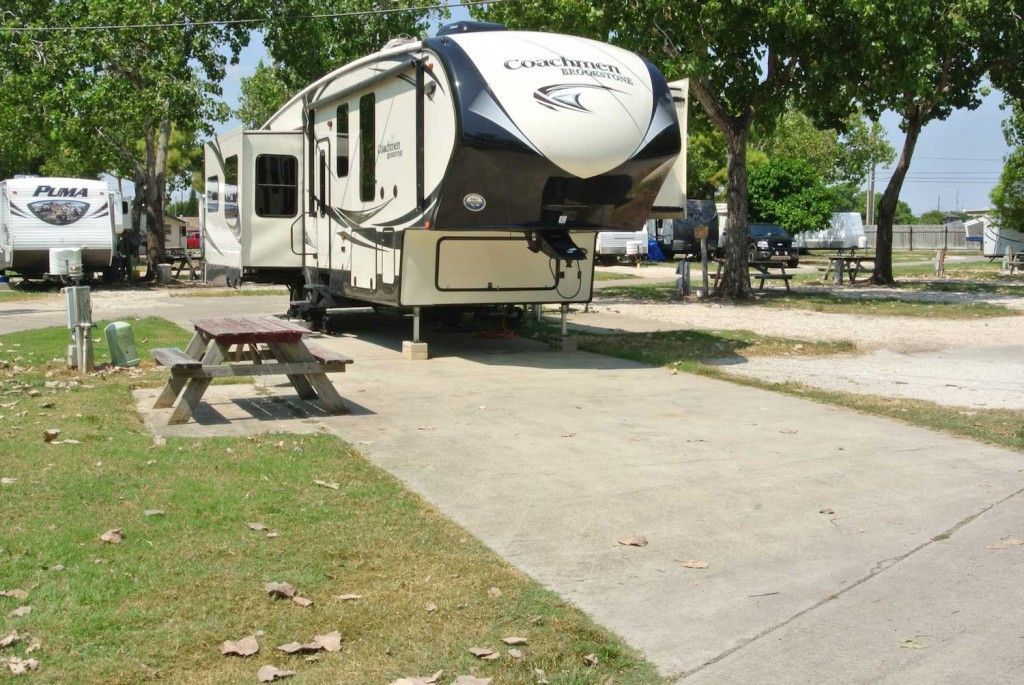 A rv is parked in a parking lot next to a picnic table.