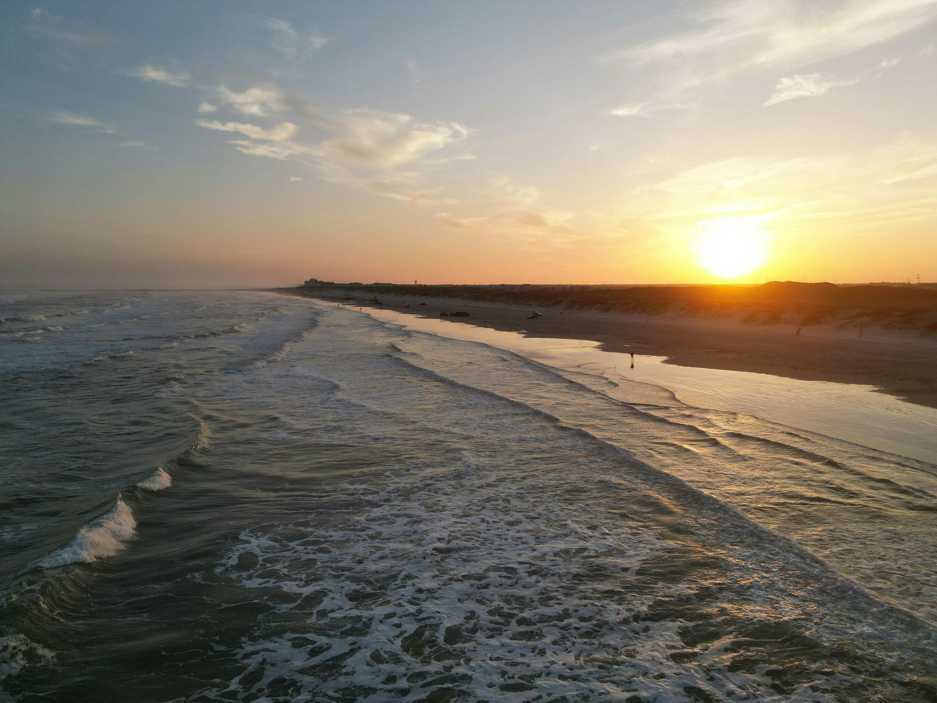 The sun is setting over the ocean and the waves are crashing on the beach.
