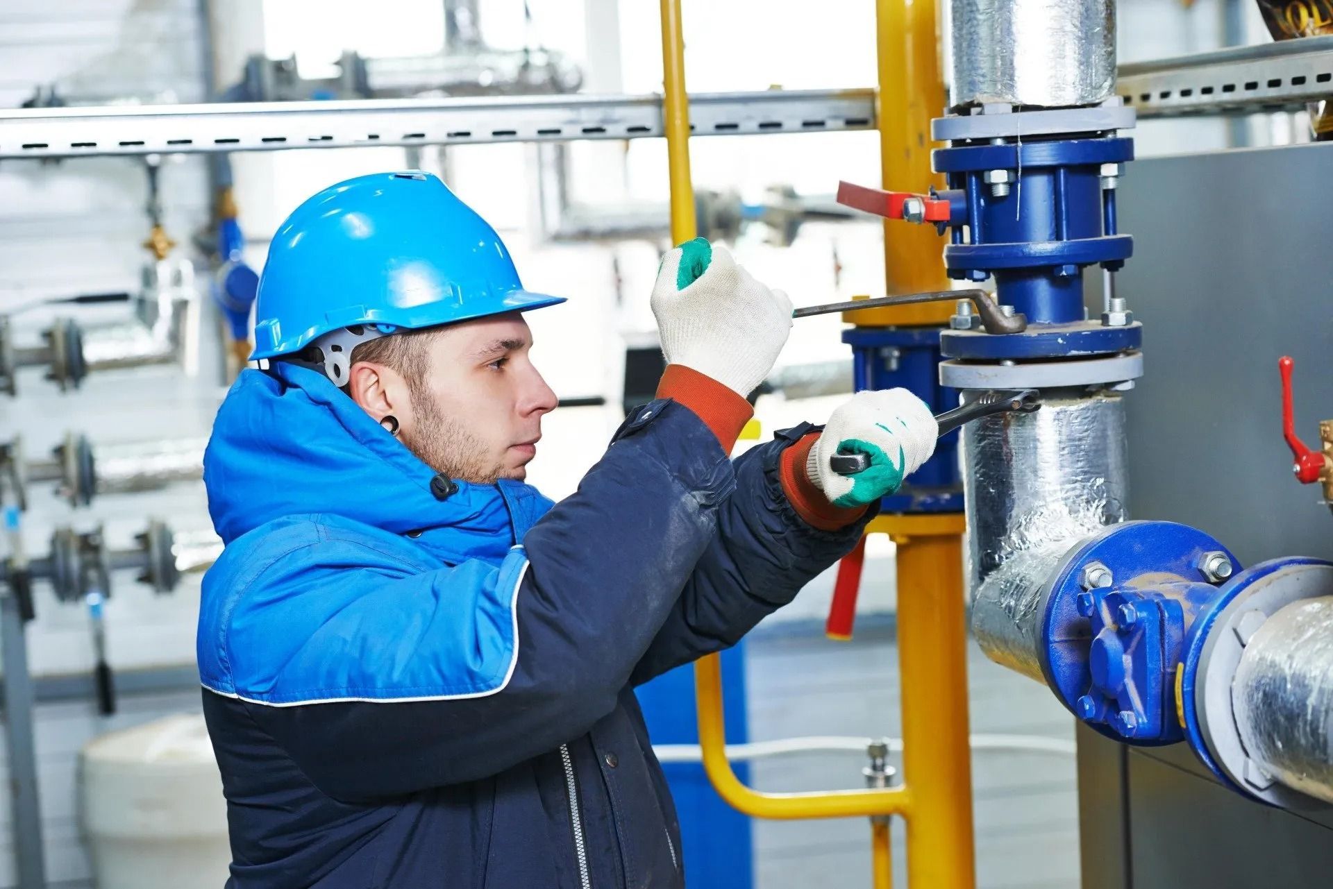 A Person Wearing a Blue Hard Hat and Gloves Works on A Blue Valve on Pipes — Weav Plumbed in Emerald, QLD