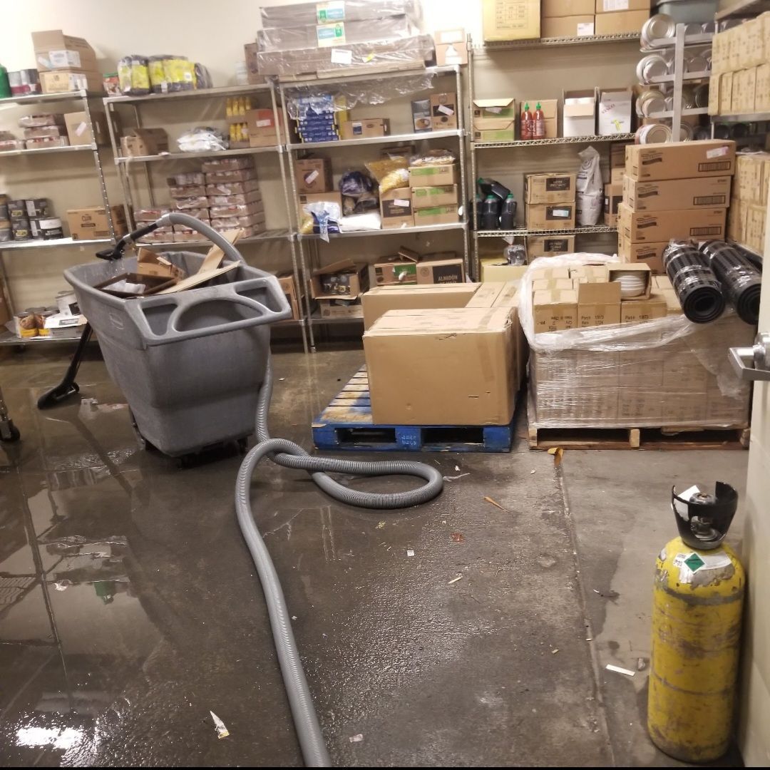 Flooded warehouse with boxes, shelving, a cart, and a gas cylinder.