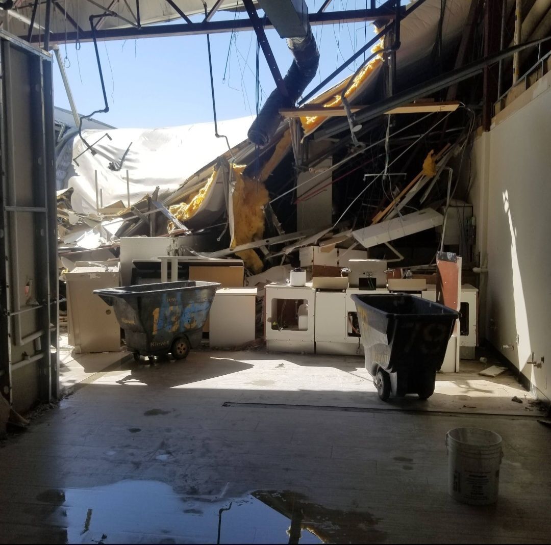 A damaged building interior with collapsed roof debris, two carts, and appliances.