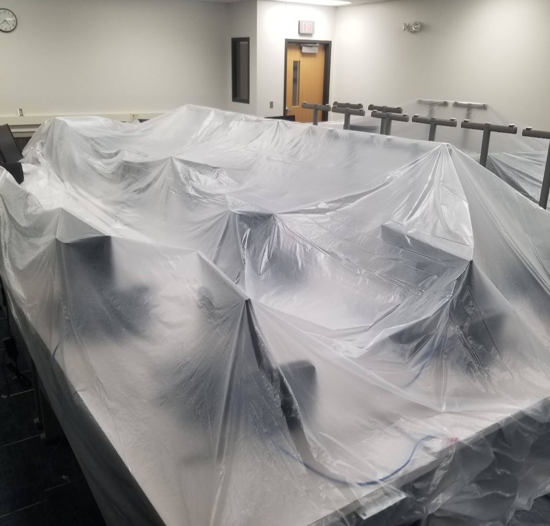 A classroom with desks covered in plastic sheeting; rows of chairs are visible in the background.